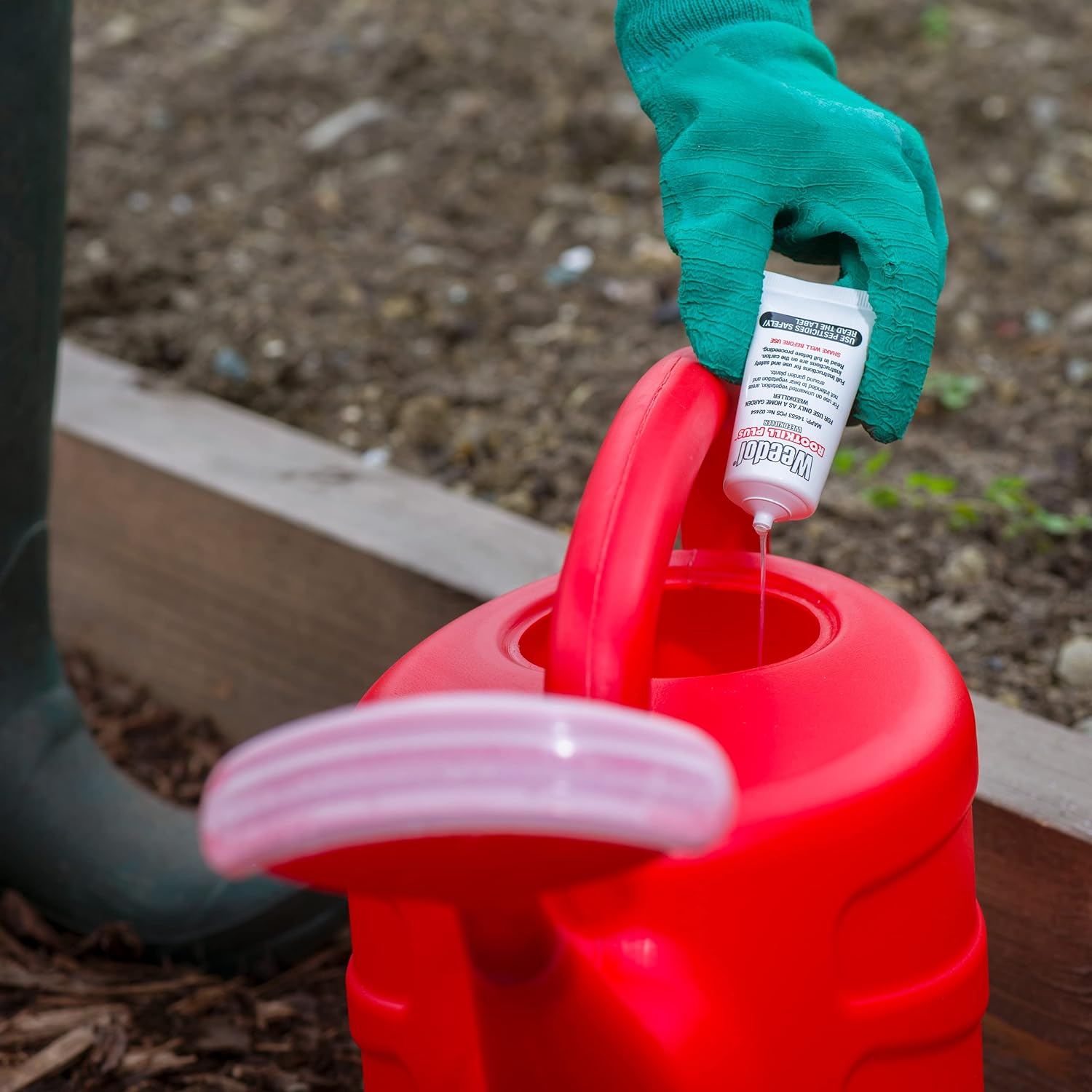 Person adding Weedol Rootkill Plus Concentrated Tubes 500ml to a red watering can for weed control in the garden.