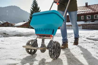 Person using GARDENA Spreader XL on snowy surface to distribute salt or grit during winter season